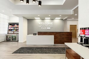Un espace d’accueil d’hôtel au design moderne, comprenant un comptoir d’accueil, un panneau mural, un mini-bar et un coin café.