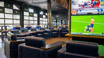 A sports bar with leather seating, large windows, and a TV screen displaying a soccer game.