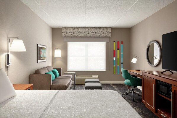 A hotel room with a bed, a desk, a chair, a TV, and a window.