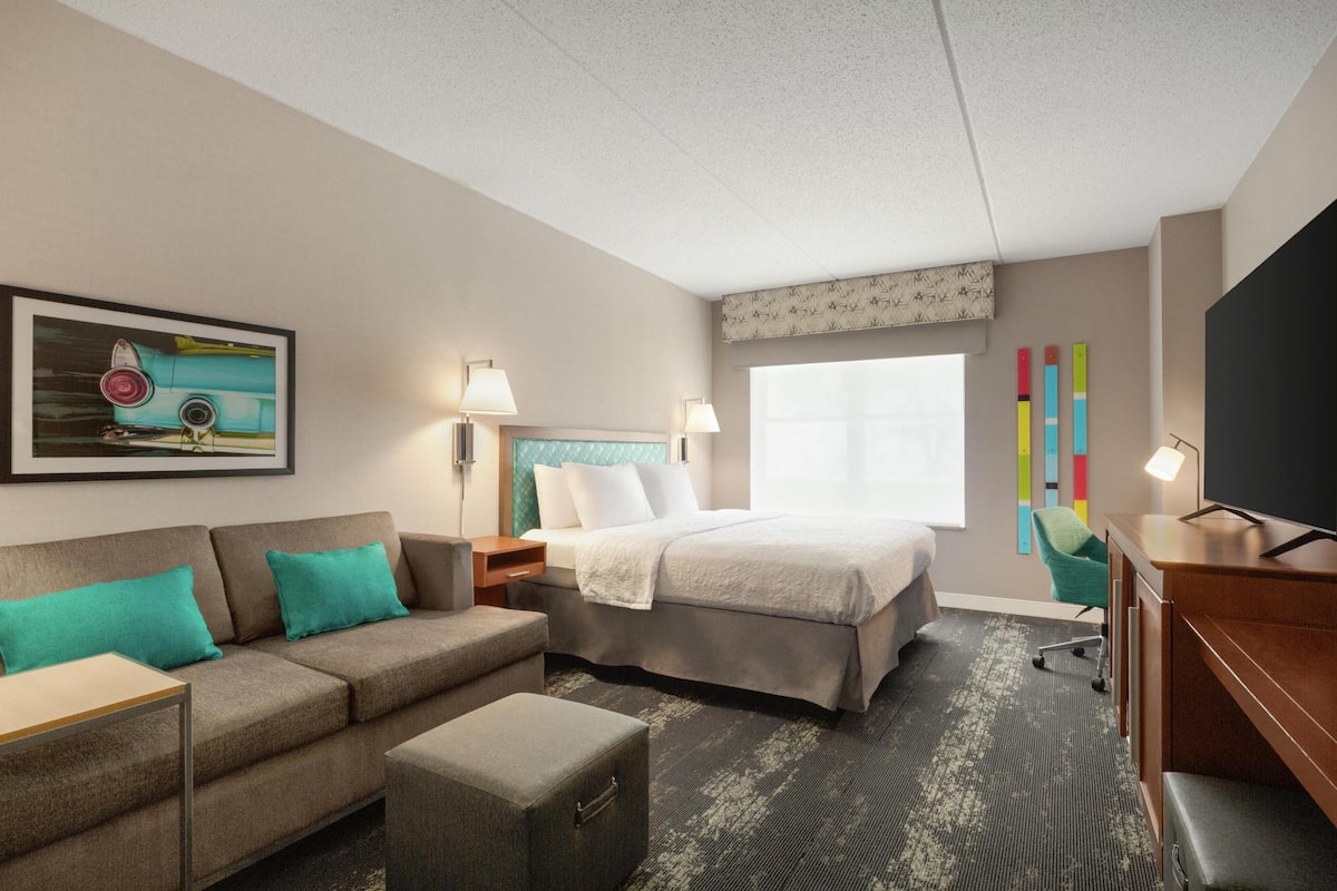 Habitación de hotel con cama, sofá, escritorio, televisor y ventana.