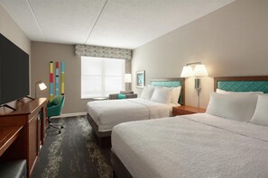 A hotel room with two beds, a desk, a TV, a window with blinds, and a colorful wall decoration. - Hampton Inn Deadwood at Tin Lizzie Gaming Resort (Deadwood)