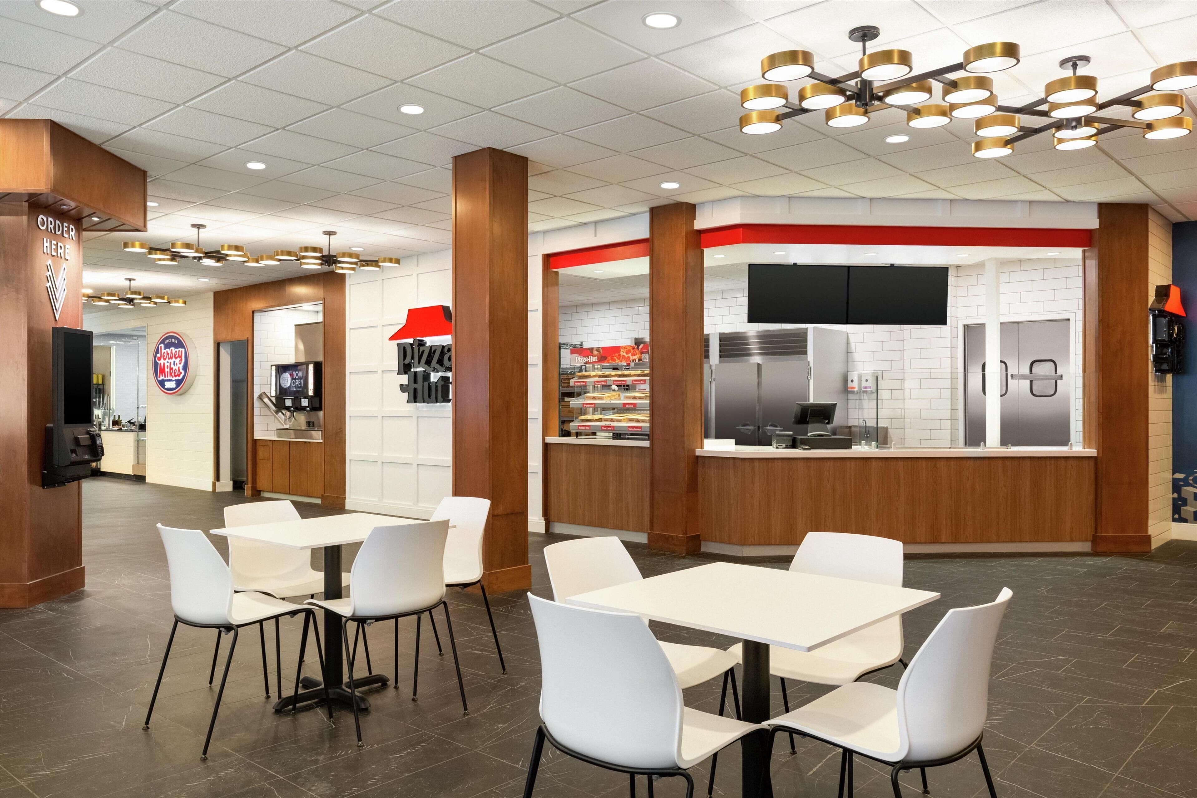A modern restaurant interior with white tables and chairs, a kitchen area, and a counter with a menu display.
