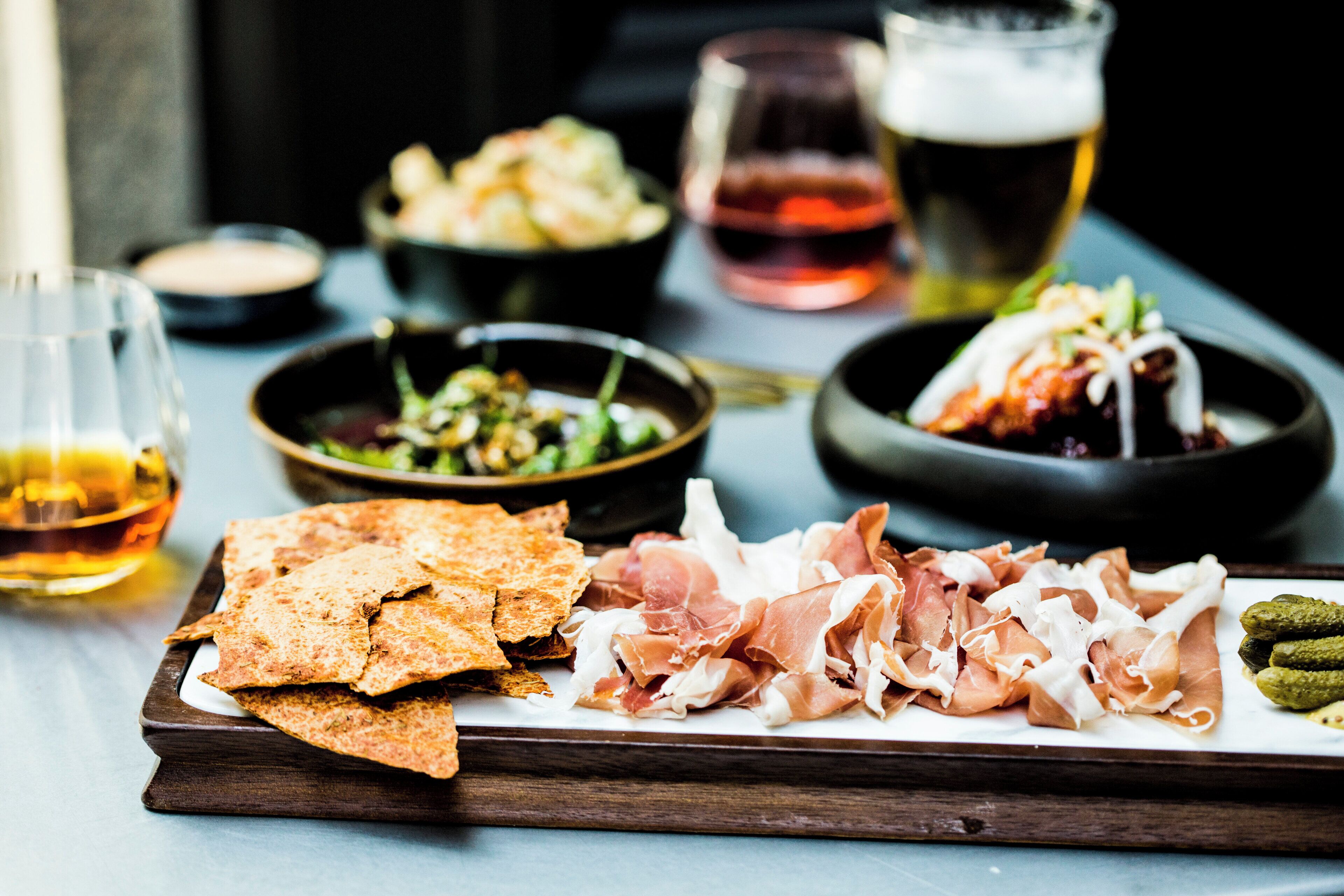 A wooden board with various food items including flatbreads, cured meats, and pickles.