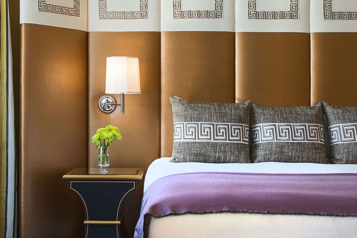 A hotel room with a bed, a nightstand, a lamp, and a vase with flowers.
