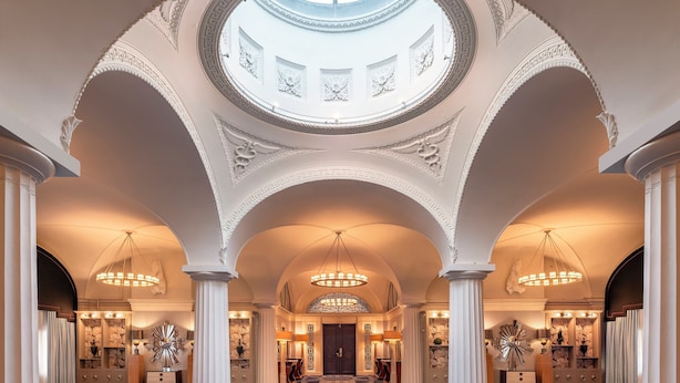 Un vaste hall d’entrée avec un plafond haut, des colonnes richement décorées et une verrière.