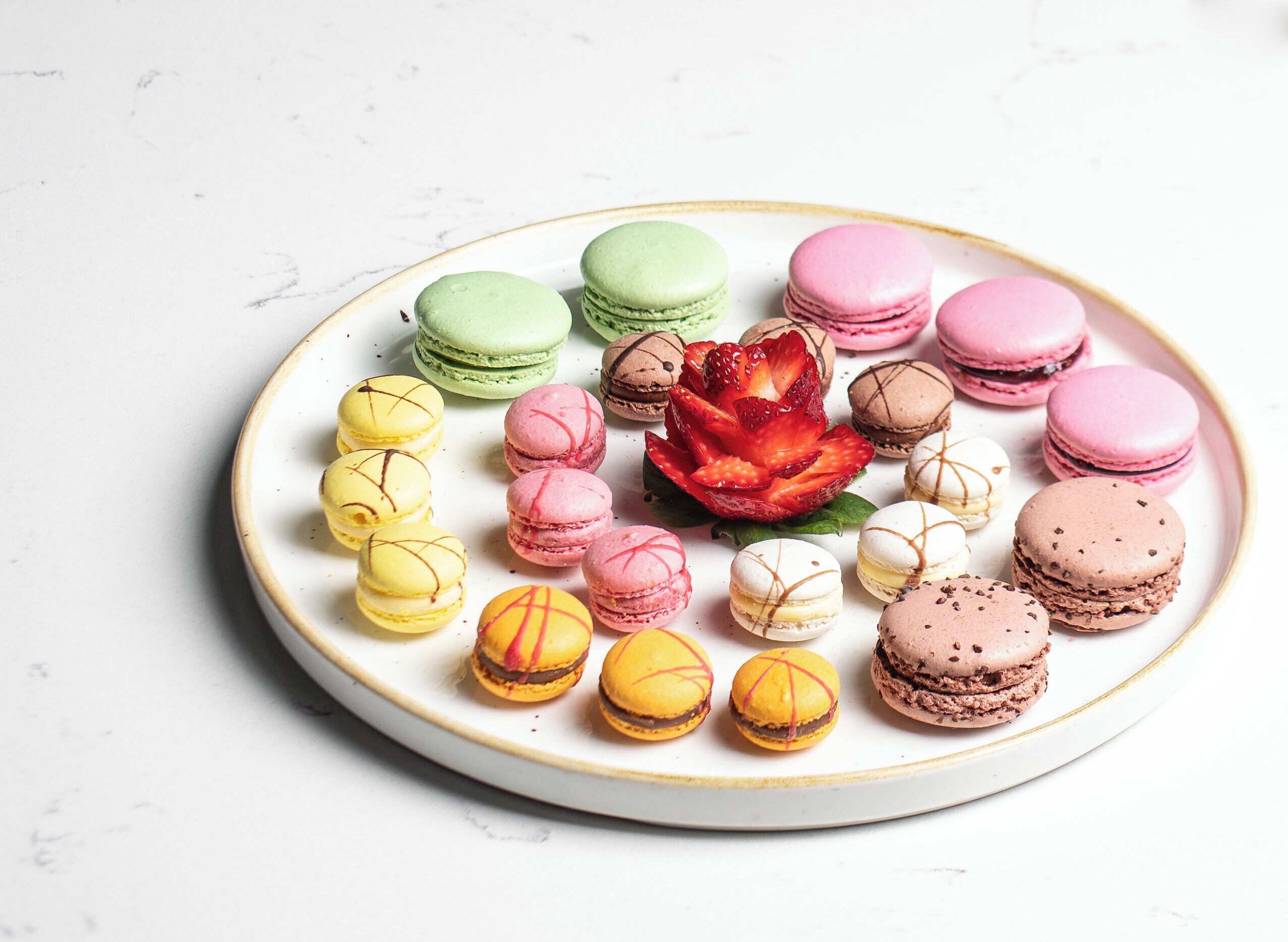 A plate of colorful macarons arranged on a white plate with a gold rim.