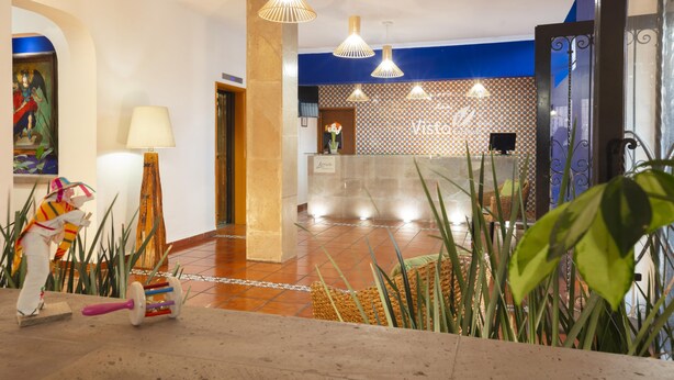 A hotel lobby with a reception desk, a large decorative sculpture, and hanging pendant lights. - Hotel Vista Express Morelia By Arriva Hospitality Group (Morelia)