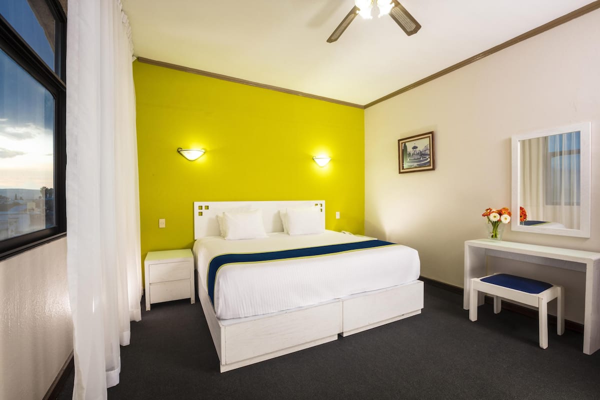 A hotel room with a bed, bedside table, and a small stool.