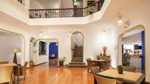 A spacious lobby with a tiled floor, multiple seating areas, a staircase, and a kitchen area visible through an archway. - Hotel Vista Express Morelia By Arriva Hospitality Group (Morelia)