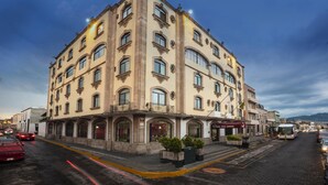 A multi-story building with a classic architectural style, featuring arched windows and a balcony on the ground floor. - Hotel Vista Express Morelia By Arriva Hospitality Group (Morelia)