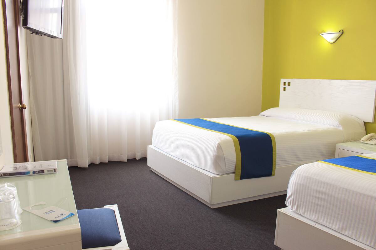 A hotel room with two beds, a desk, a telephone, and a wall-mounted light fixture.