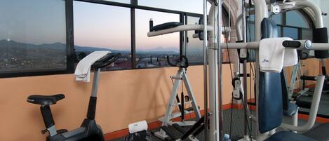 A gym with exercise equipment, a treadmill, and a view of a cityscape through large windows.