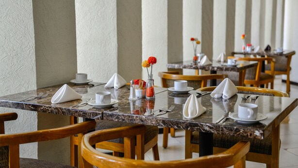 A dining area with marble tables, wooden chairs, and neatly arranged dining ware.