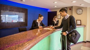 A reception desk in a hotel lobby with a blue accent wall, a clock, and a framed certificate on the wall.