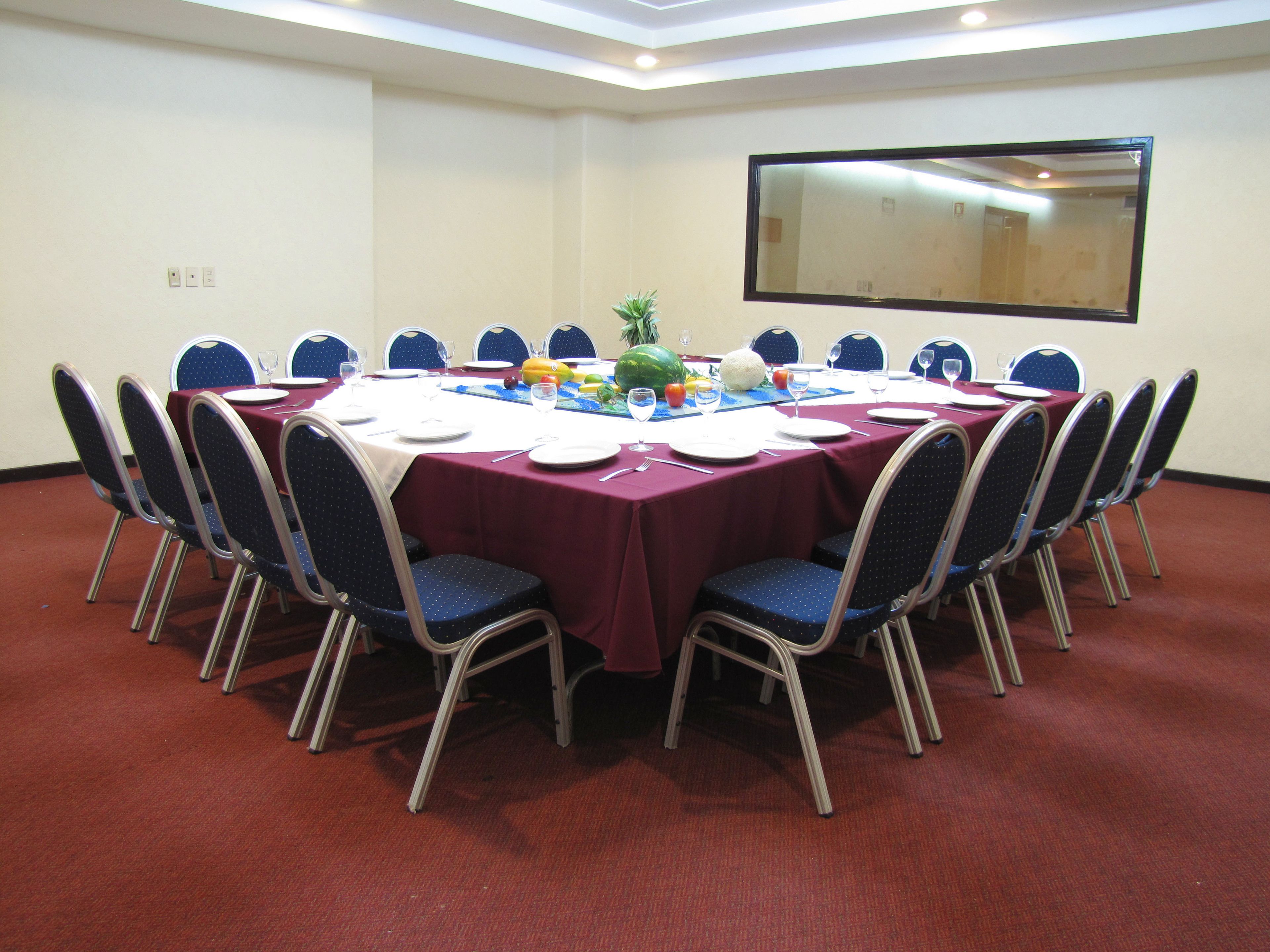 Un salón de conferencias con una mesa redonda, sillas azules y un mantel rojo.