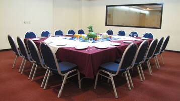 Un salón de conferencias con una mesa redonda, sillas azules y un mantel rojo.