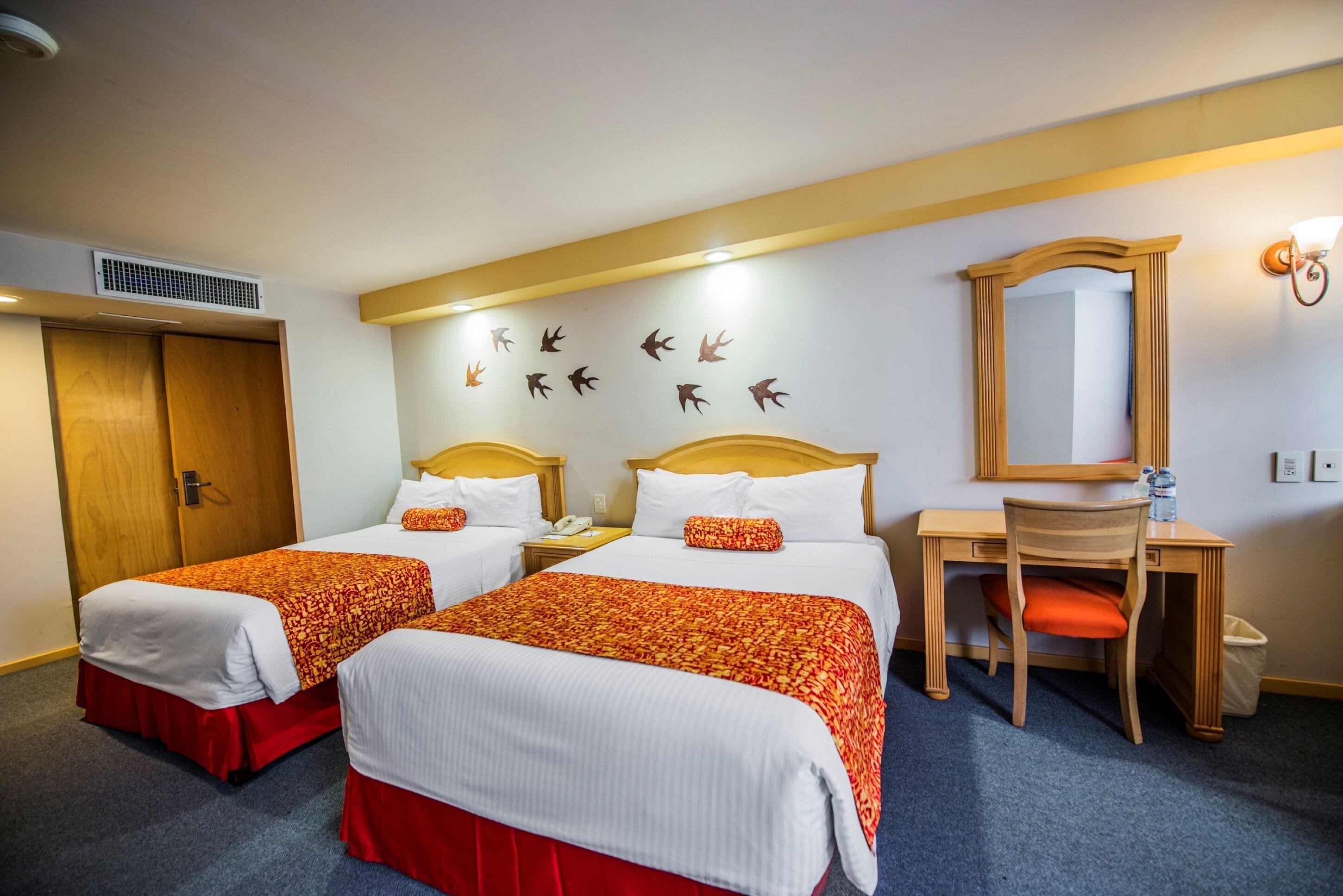 A hotel room with two beds, a desk, a chair, a mirror, and a wall with animal silhouettes.