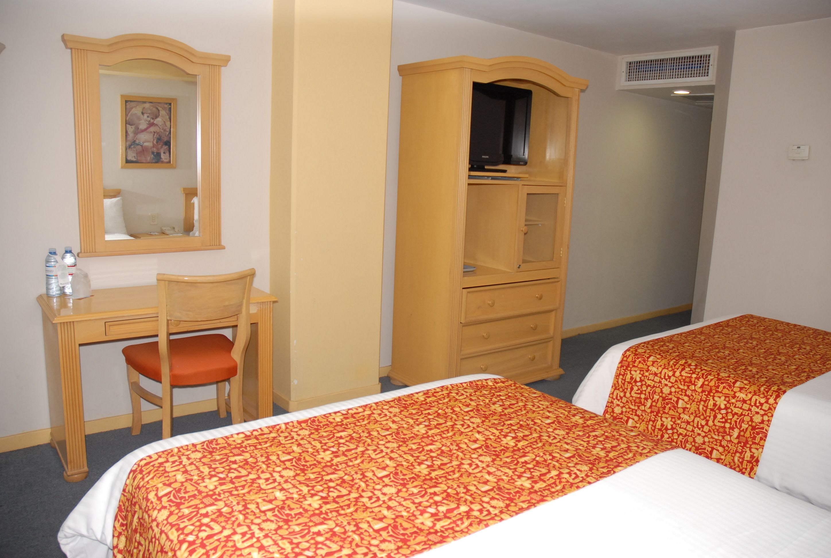 Une chambre d’hôtel avec deux lits, un bureau avec une chaise, une armoire et un miroir.