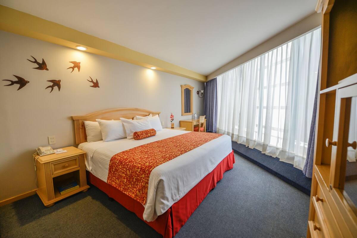 Een hotelkamer met een groot bed, een nachtkastje, een spiegel en een raam met gordijnen.
