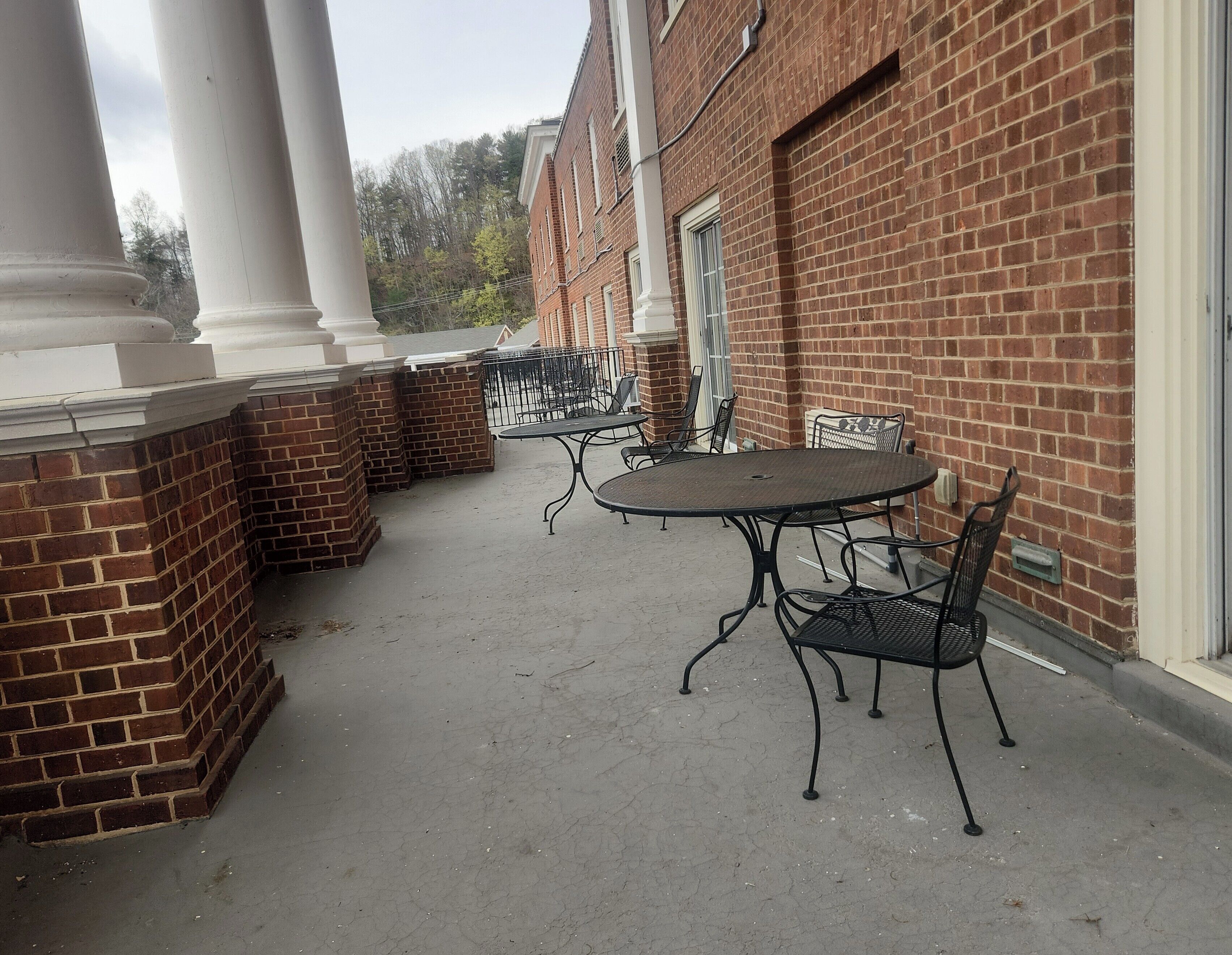 An outdoor patio area with a round metal table and chairs, brick walls, and white columns.
