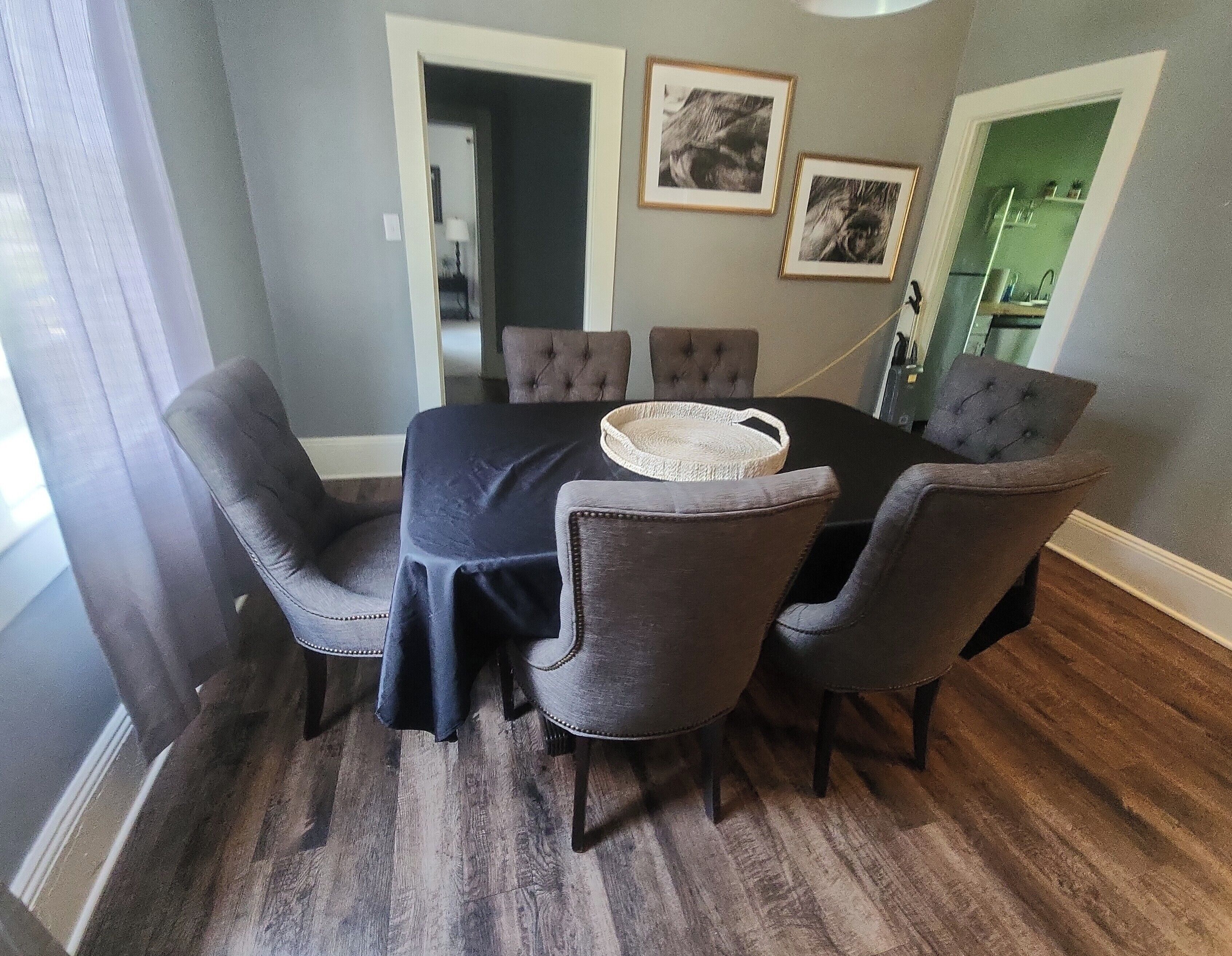 A dining area with a round table, dark tablecloth, and six upholstered chairs.