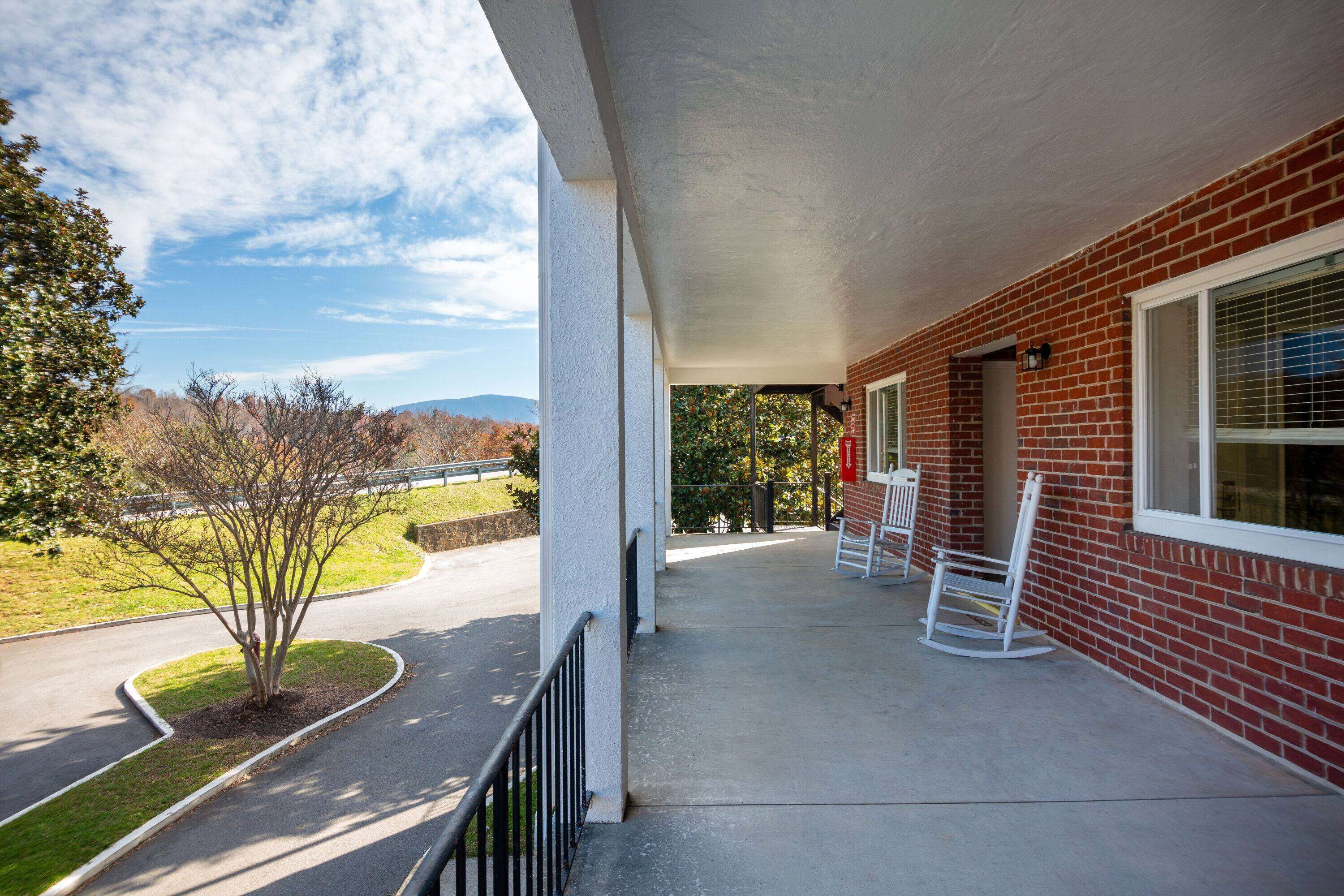 A covered porch with a brick building, a small tree, and a clear view of the road and mountains in the background.