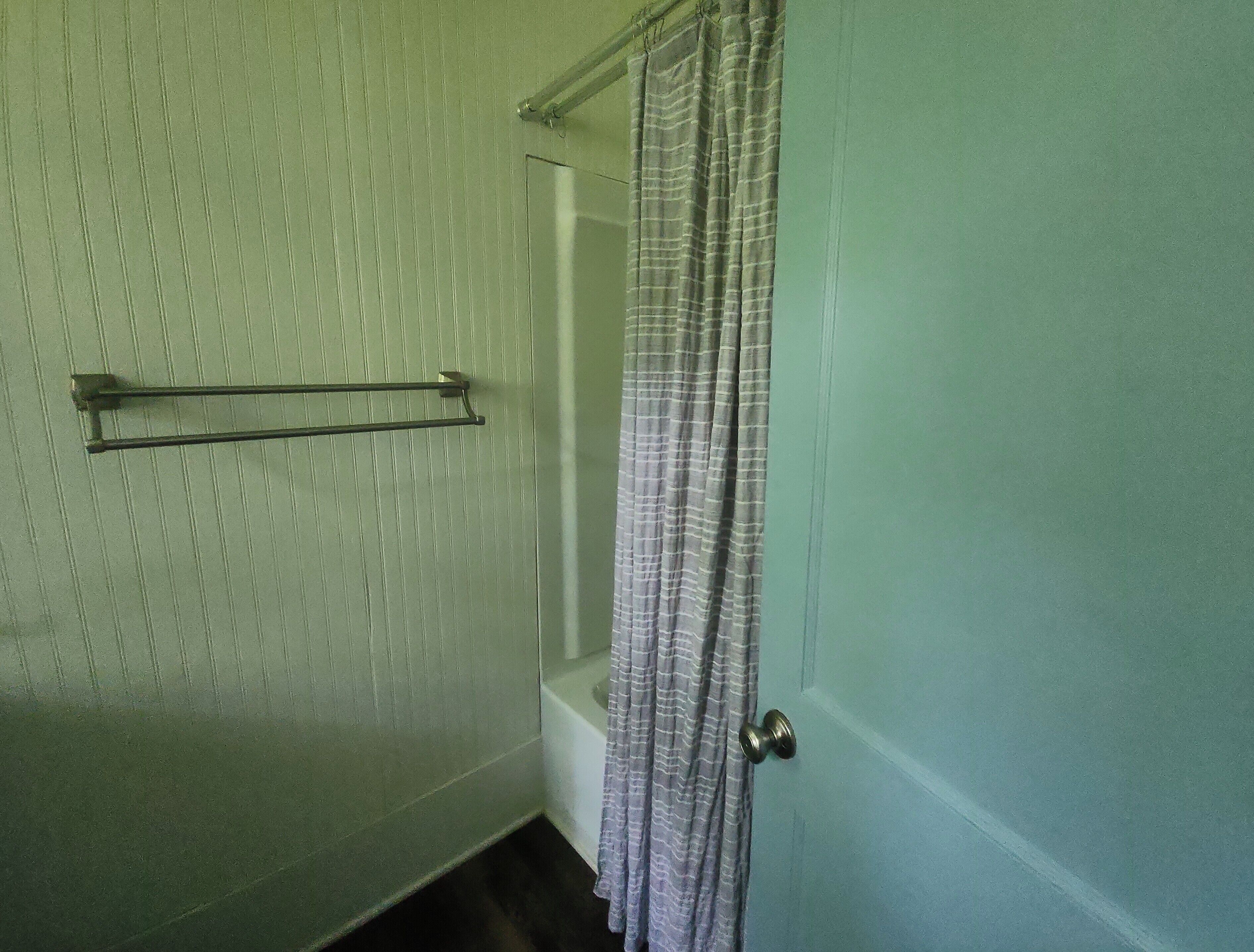 A bathroom with a shower curtain, a towel rack, and a door.
