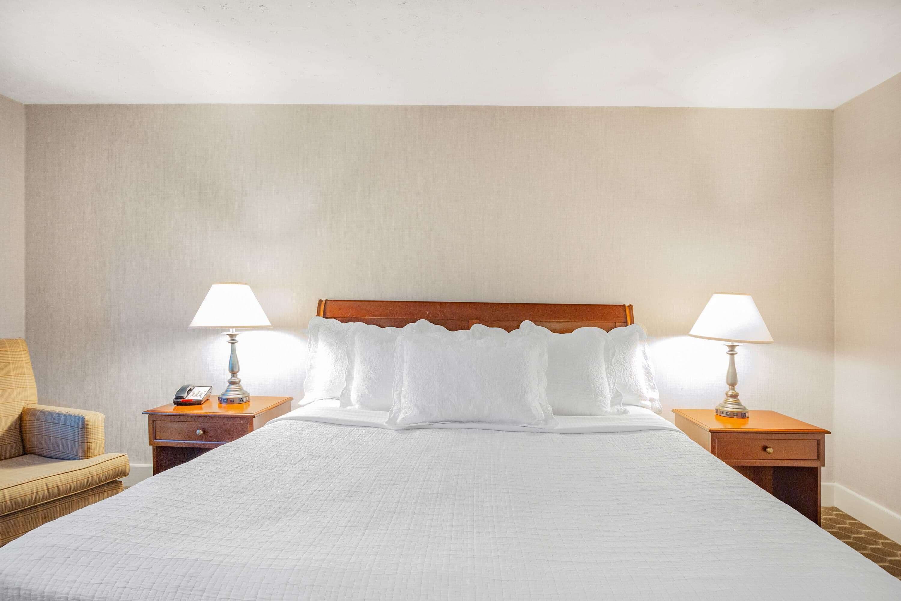 Una camera d'albergo con un letto grande, due comodini con lampade, una sedia e una testiera in legno.