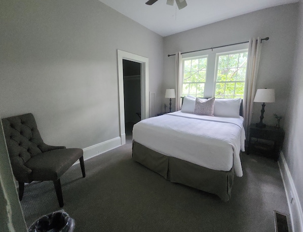 A bedroom with a large bed, a chair, a nightstand, and a window with curtains.