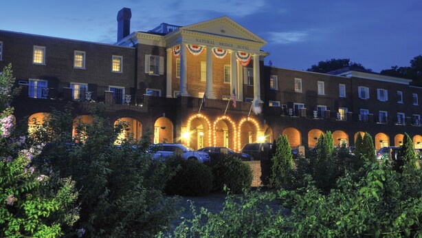 A hotel with a classical facade, arched windows, and a central entrance with a flag. - Natural Bridge Hotel, Trademark Collection by Wyndham (Natural Bridge)