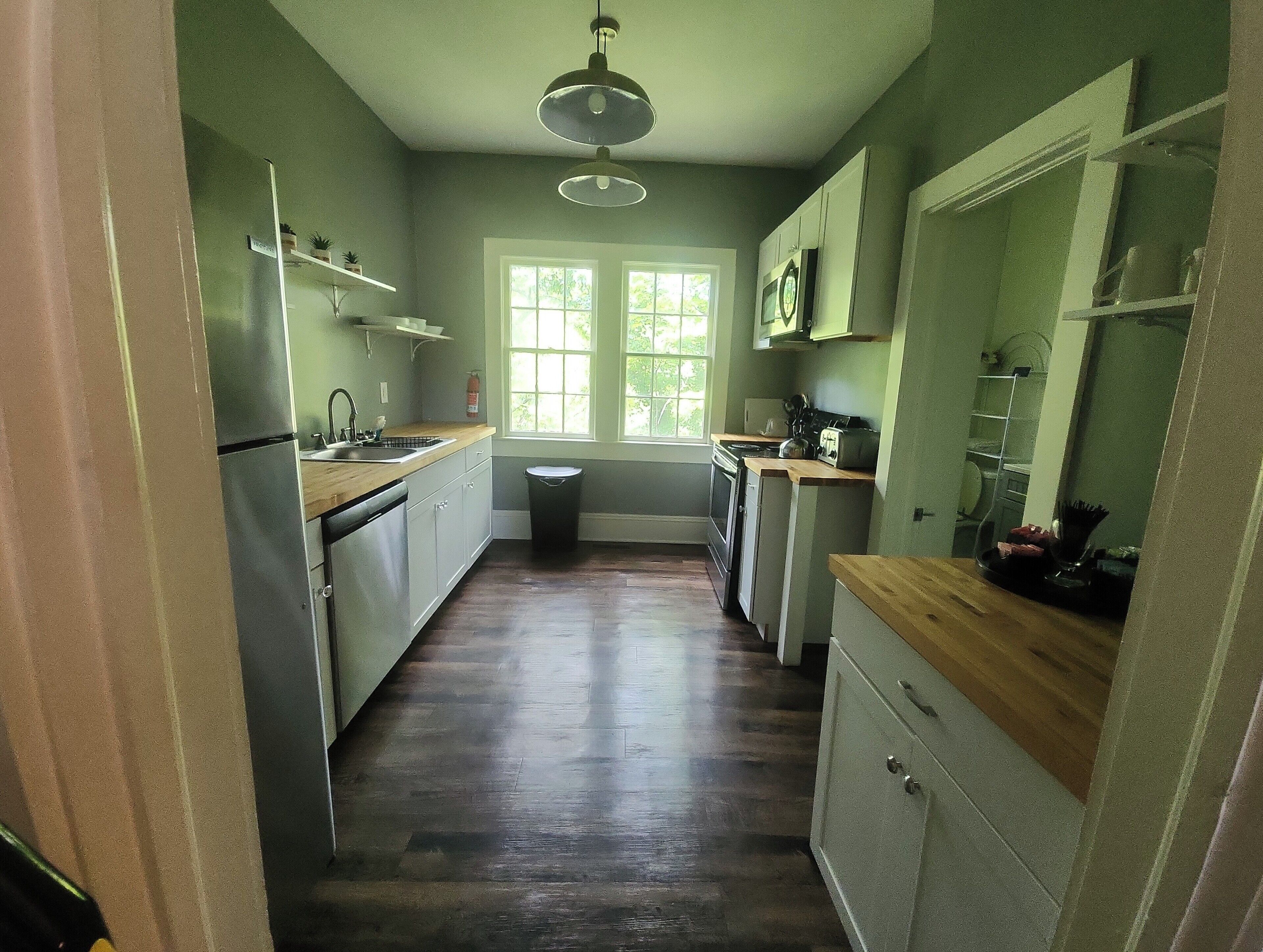 A narrow kitchen with a wooden countertop, stainless steel appliances, and a window with a view of greenery.