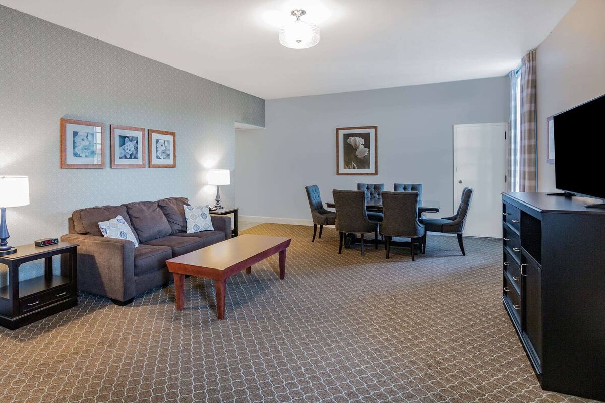 Ein Hotelzimmer mit Sofa, Couchtisch, Fernseher, Esstisch mit Stühlen und einem Schrank.