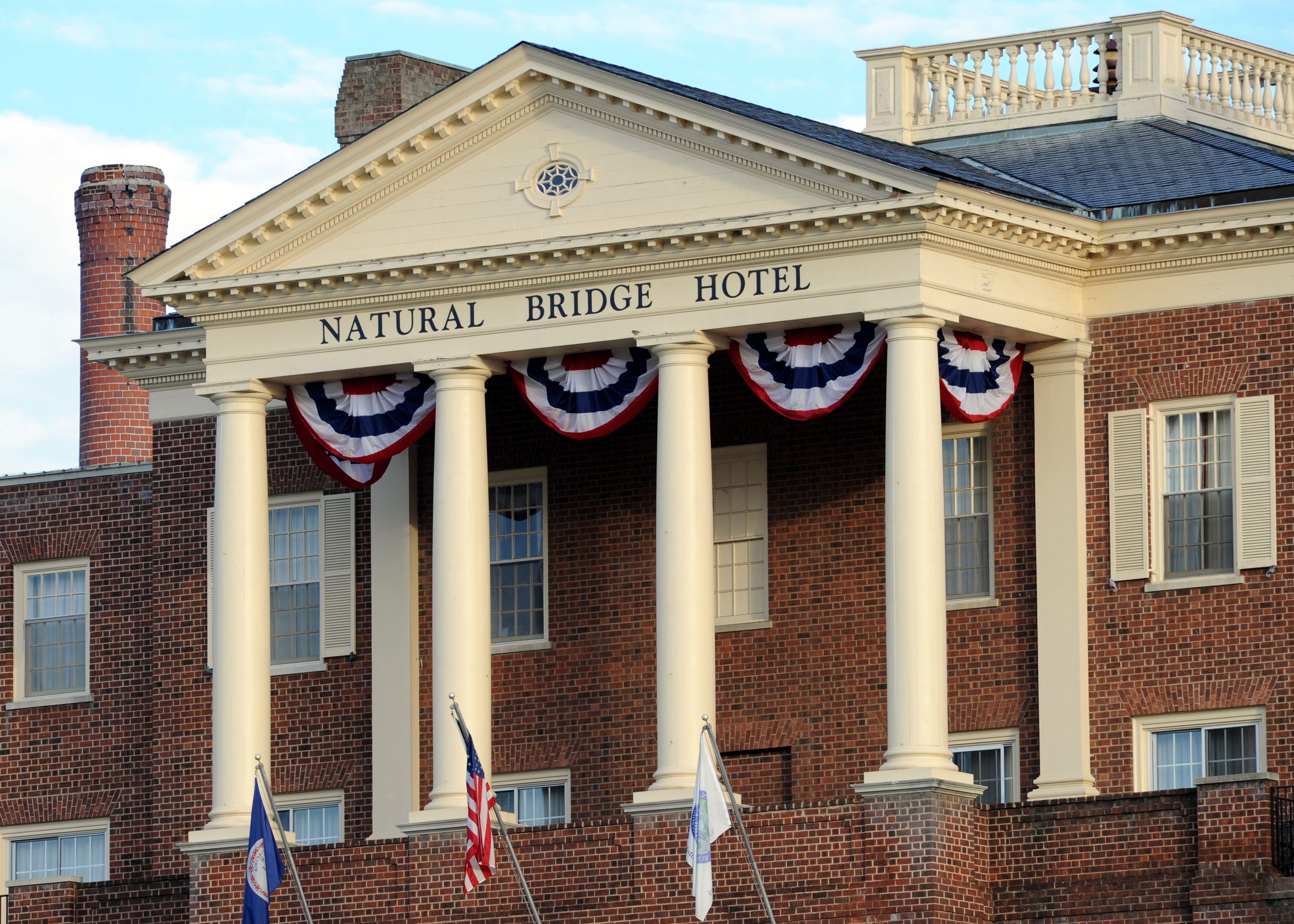A hotel facade with the name "NATURAL BRIDGE HOTEL" above the entrance, featuring a classical architectural style with columns and a decorative pediment.