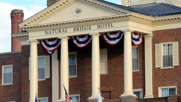 La façade d’un hôtel, sur laquelle on peut lire l’inscription « NATURAL BRIDGE HOTEL » au-dessus de l’entrée, présente un style architectural classique avec des colonnes et un fronton décoratif.