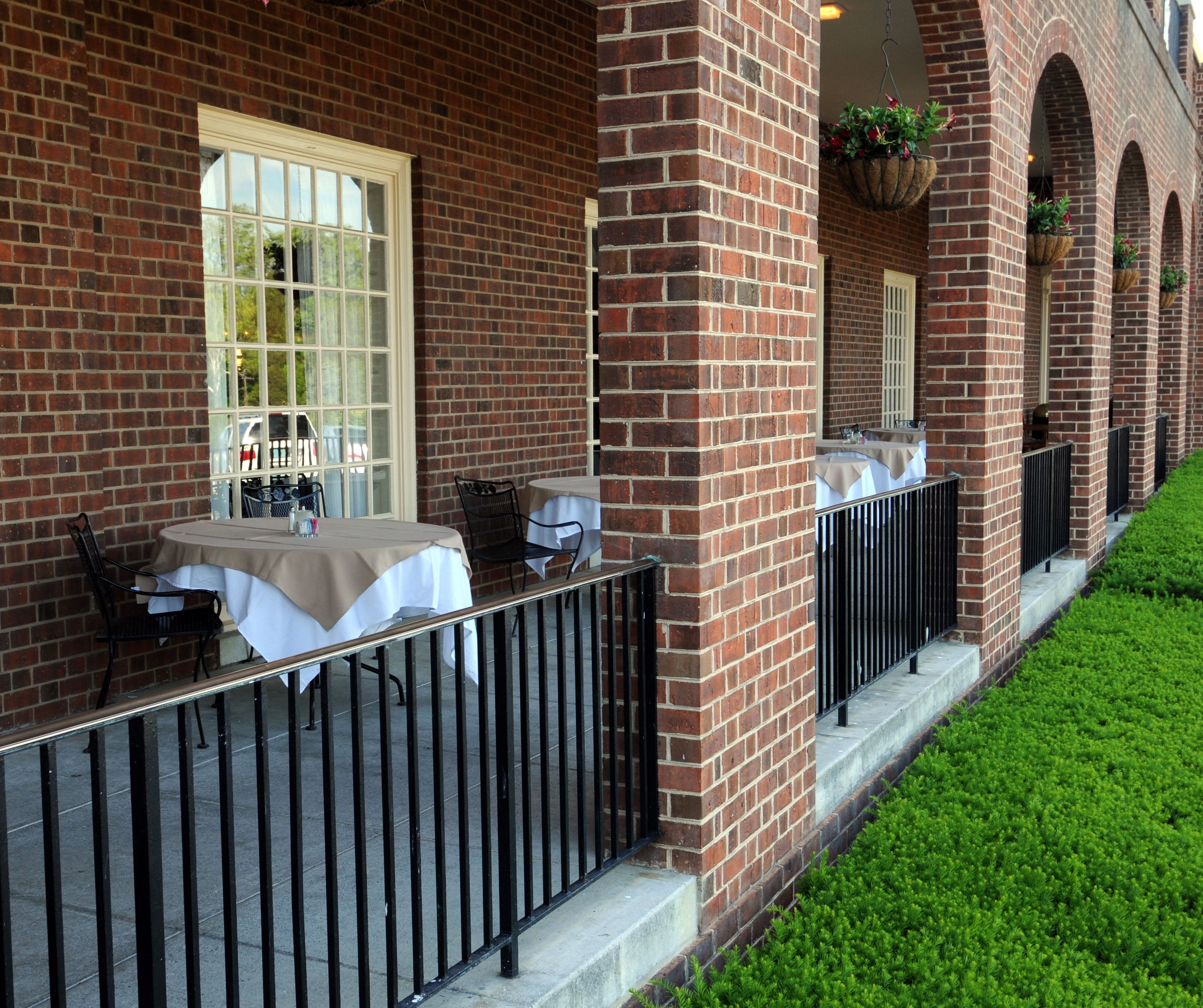 A brick building with outdoor seating, white tablecloths, and black metal railings.