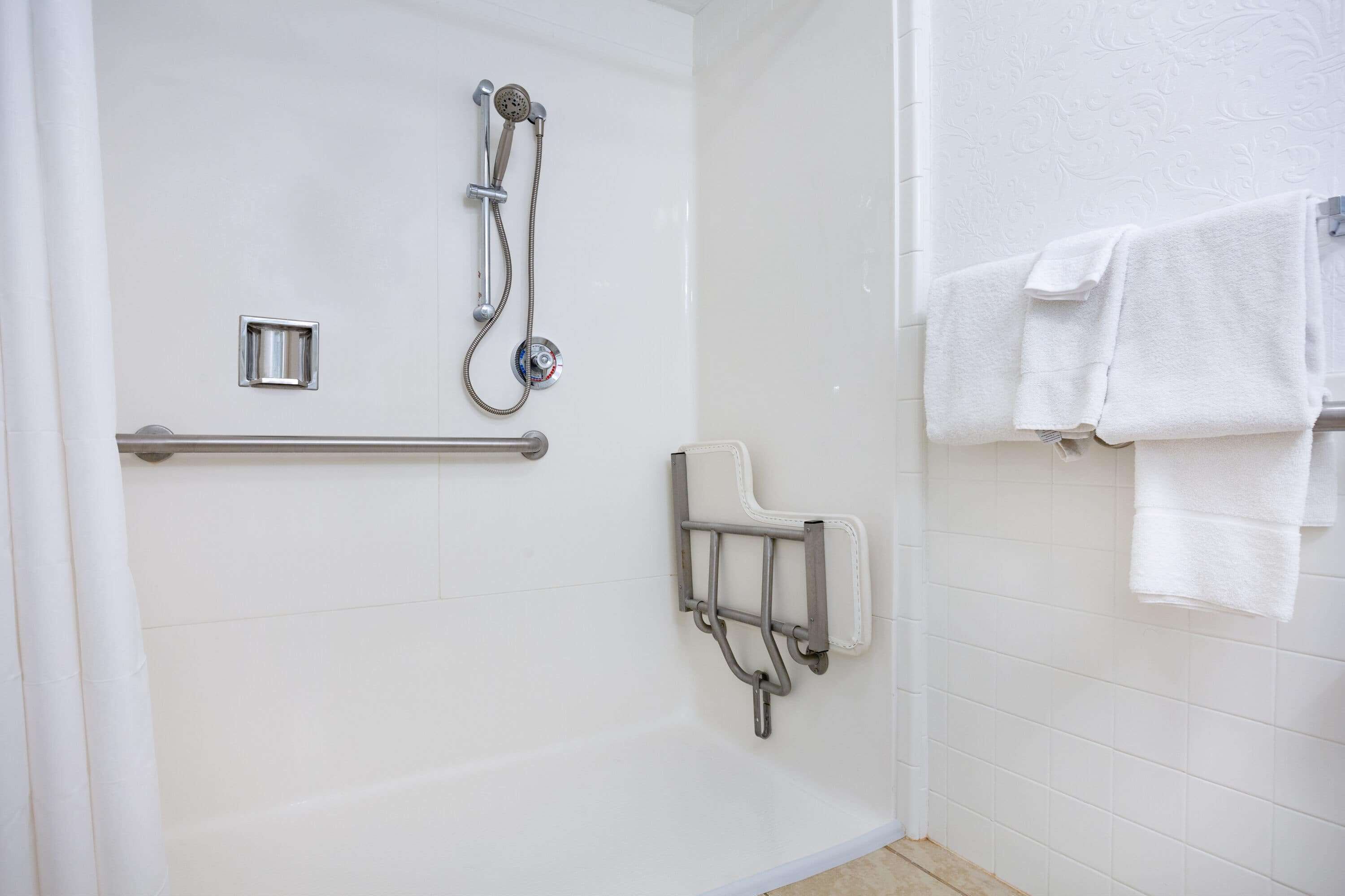 A shower area with a handheld showerhead, a handheld shower attachment, and a grab bar.