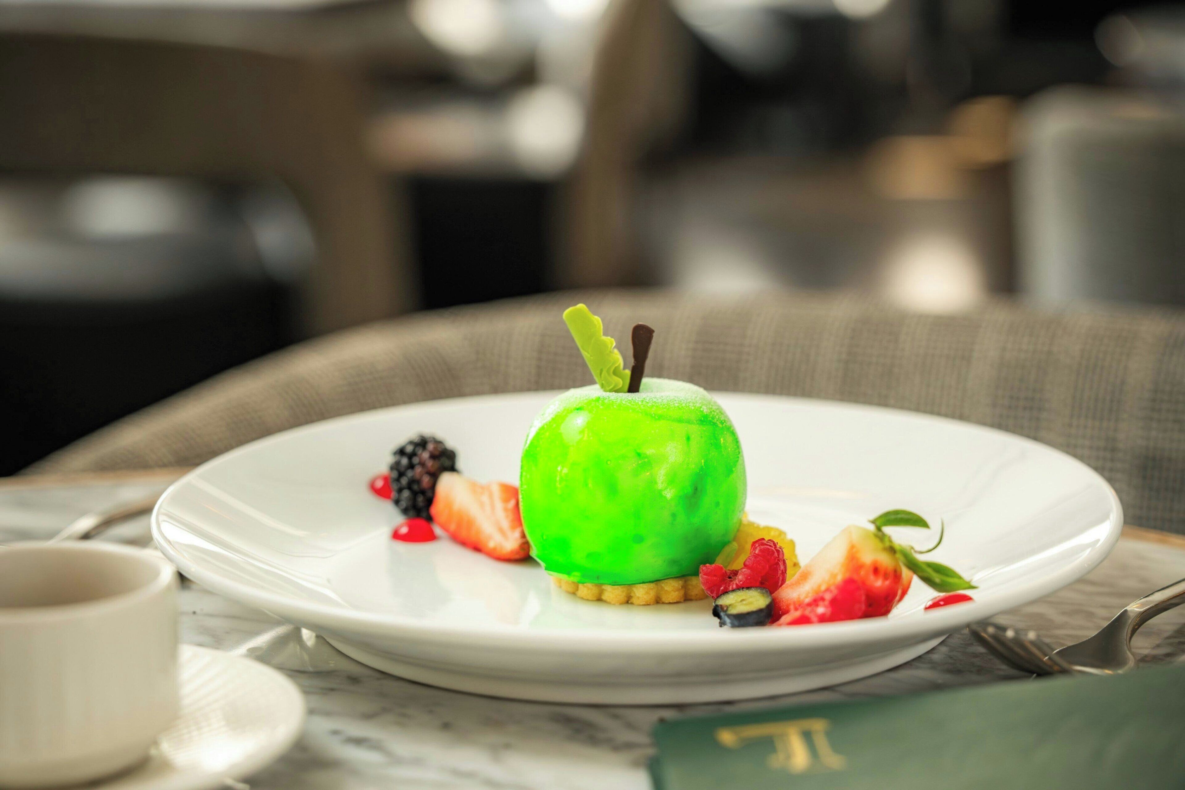 Un dessert servi dans une assiette blanche, composé d’une pomme verte, de fraises et de baies.