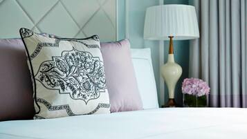 A neatly made bed with patterned pillows, a bedside lamp, and a vase with flowers.