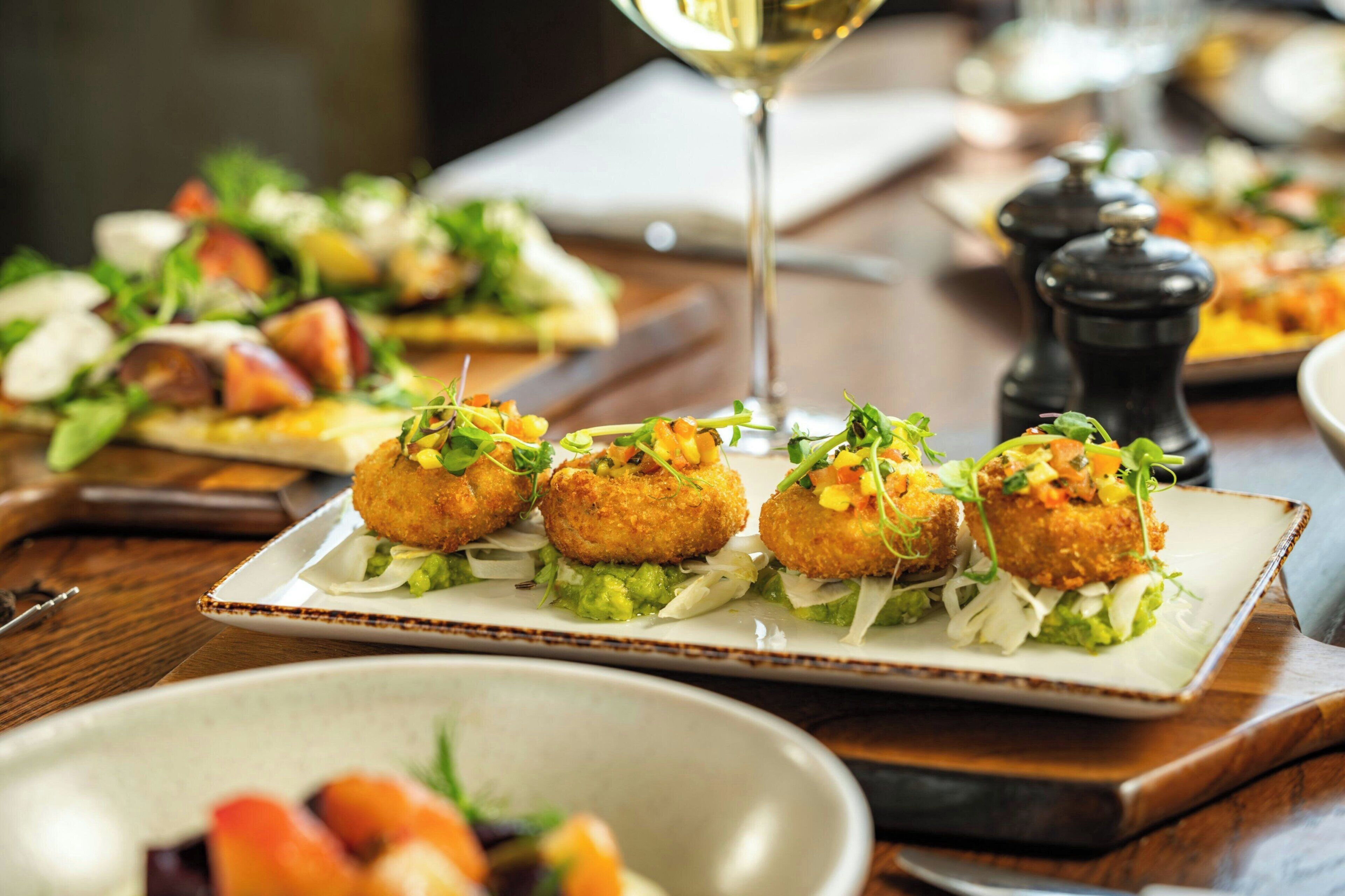 A dining table with a plate of appetizers, a wine glass, and salt and pepper shakers.