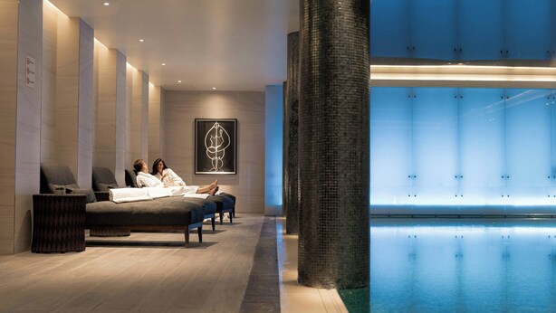 A modern spa area with a large indoor pool, seating area with massage tables, and a large pillar. - London Marriott Hotel Park Lane (London)