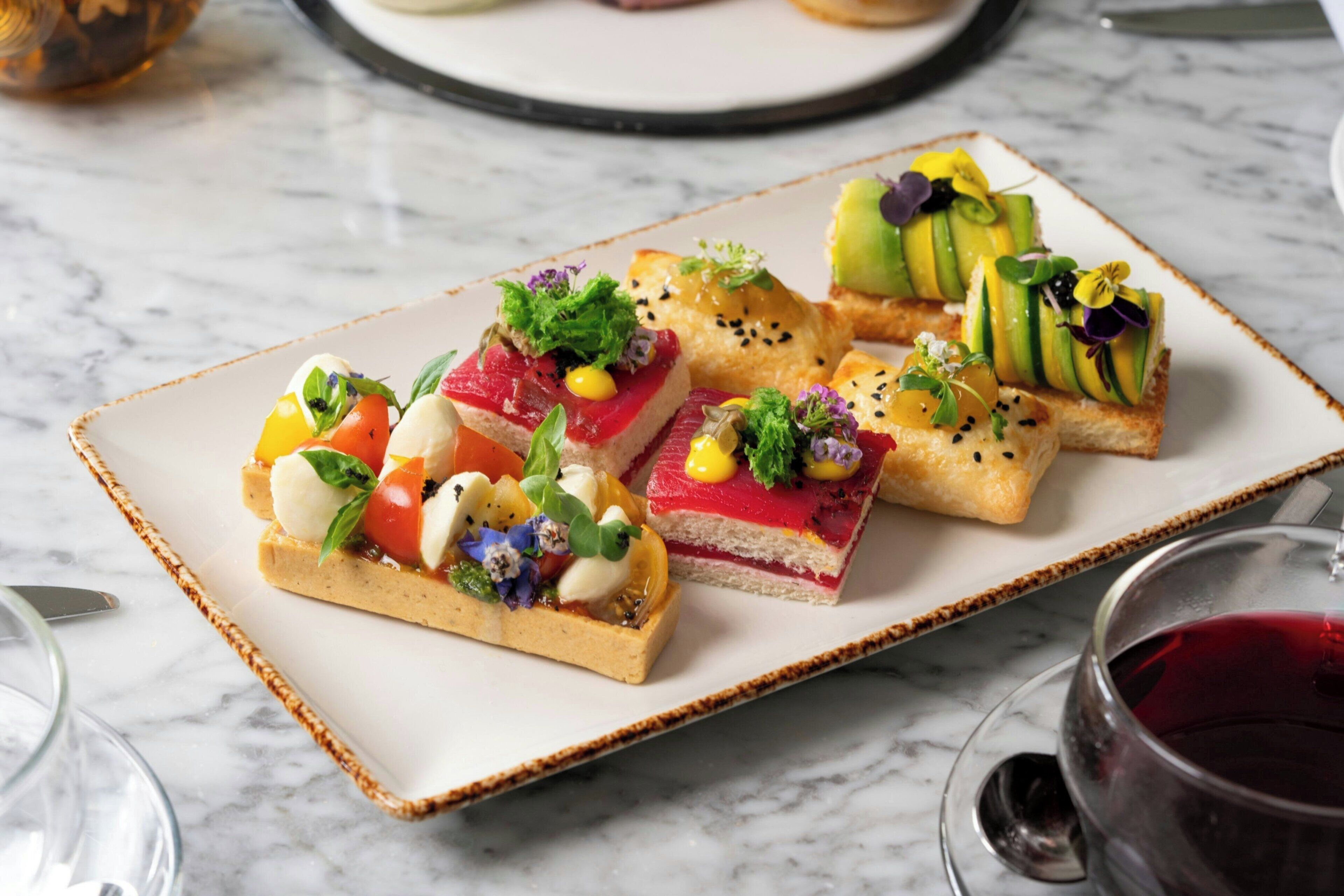 A plate of appetizers with various toppings, including vegetables and possibly seafood, on a marble table.