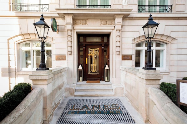 Una entrada imponente con una puerta de madera, dos faroles negros y un felpudo que dice "LANES OF LONDON".