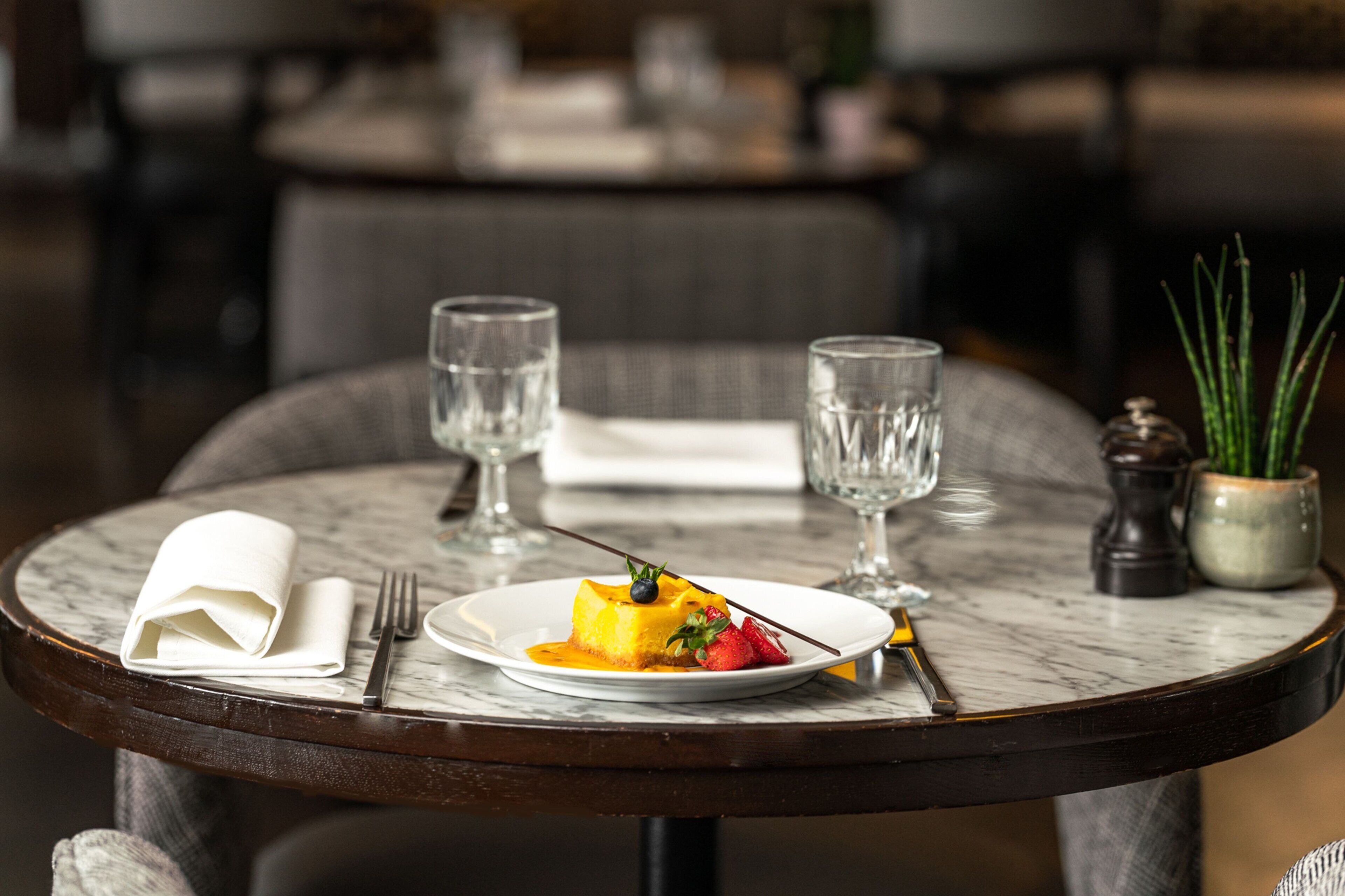 A dining table with a dessert plate, two glasses, a folded napkin, and a salt and pepper shaker.