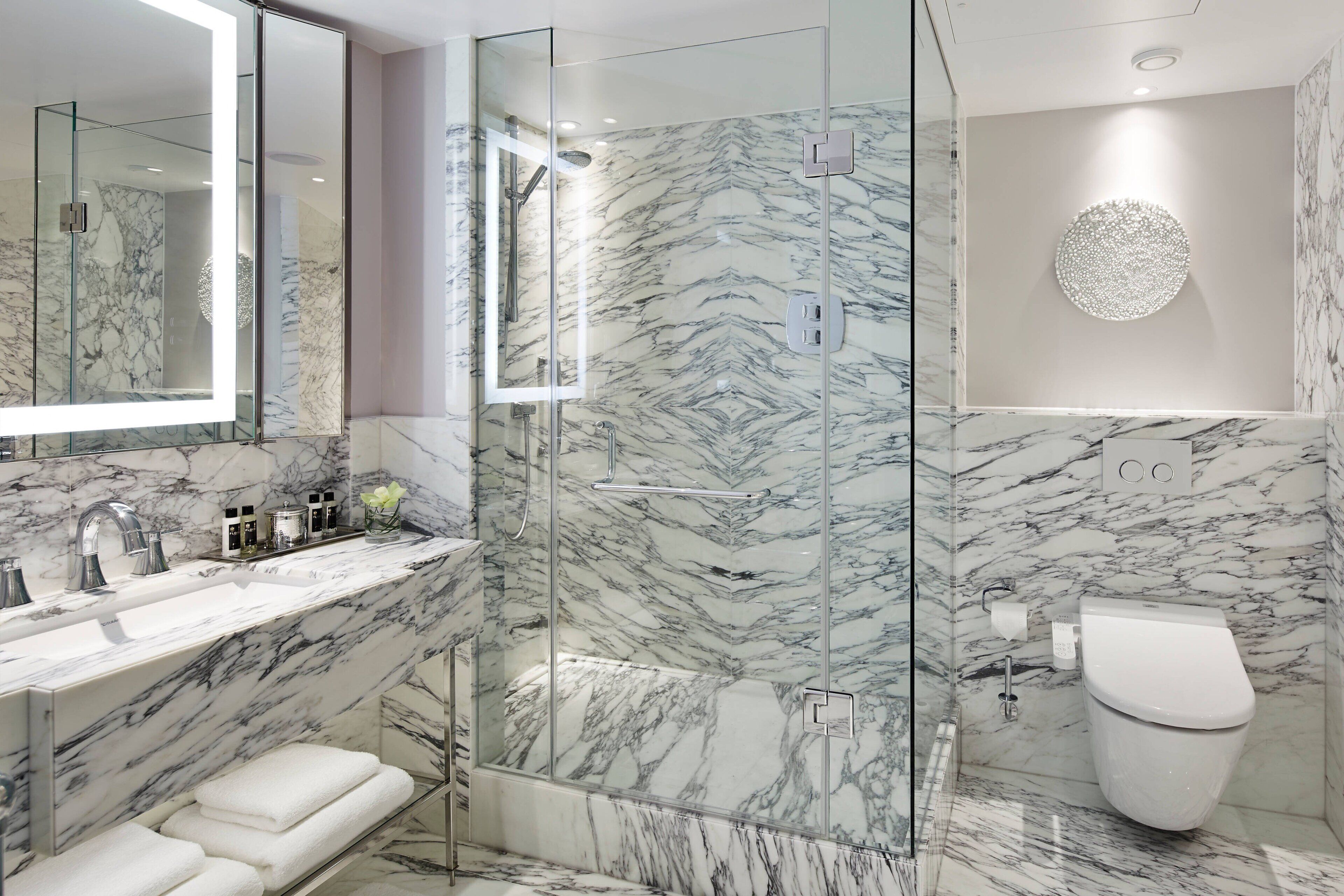 A modern bathroom with a glass-enclosed shower, marble walls, and a large mirror.