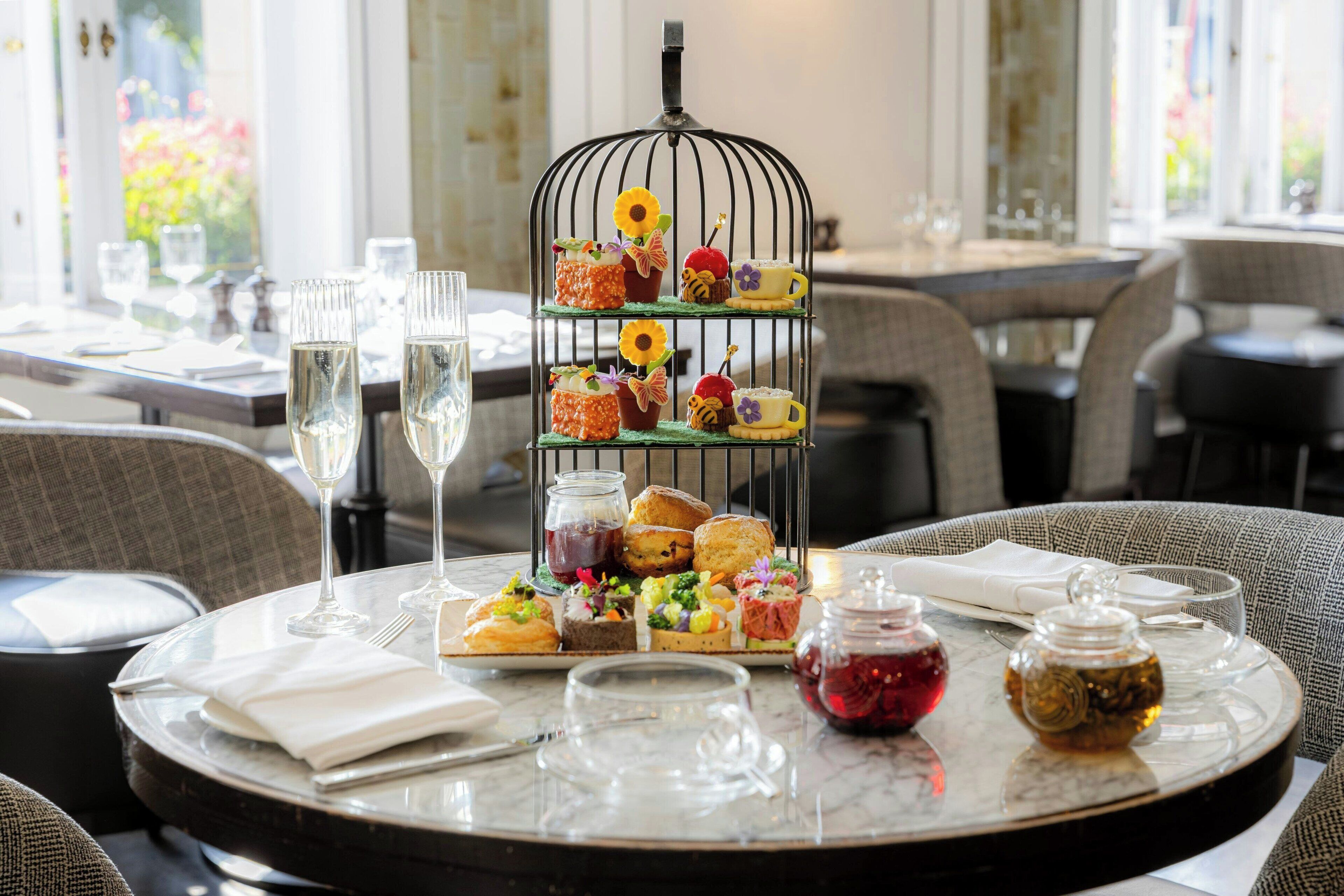 Une table à manger avec un présentoir à étages pour les desserts, des verres et un petit pot de confiture.
