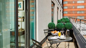 A balcony with a table set for breakfast, including croissants, a coffee pot, and a glass of orange juice. There are potted plants and a view of a red brick building in the background. - London Marriott Hotel Park Lane (London)