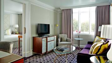 A hotel room with a large window, a sofa, a television, a small table, and a cabinet.