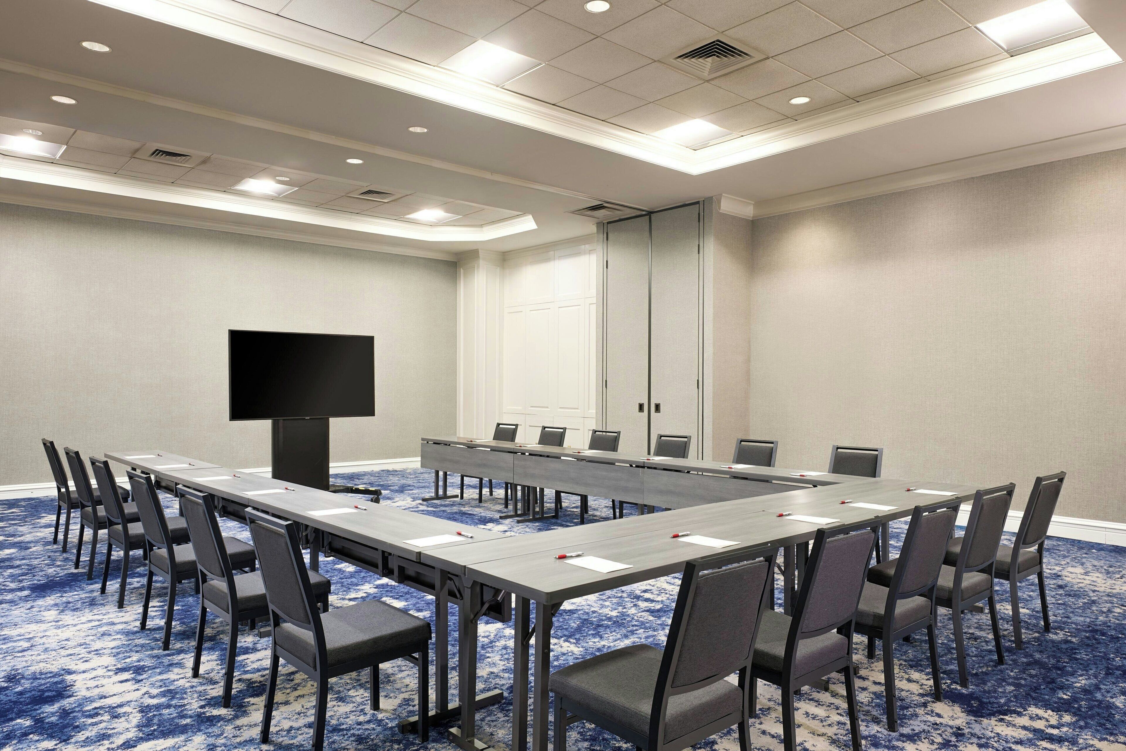 A conference room with a long table, chairs, a flat-screen TV, and a door.