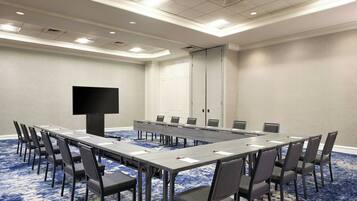 A conference room with a long table, chairs, a flat-screen TV, and a door.