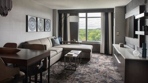A modern hotel room with a sofa, dining table, and a view of the outdoors.